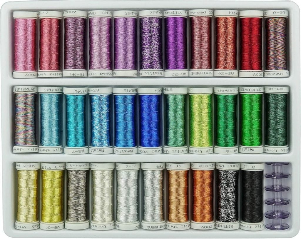 A tray containing 30 spools of thread in various colors, arranged in three rows, with four clear bobbins in the bottom right corner.