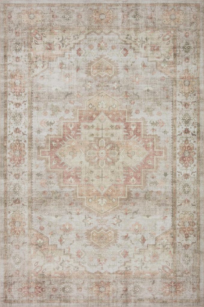 A faded, ornate area rug with a central geometric medallion design in muted shades of pink, beige, and taupe, featuring intricate floral and border patterns.