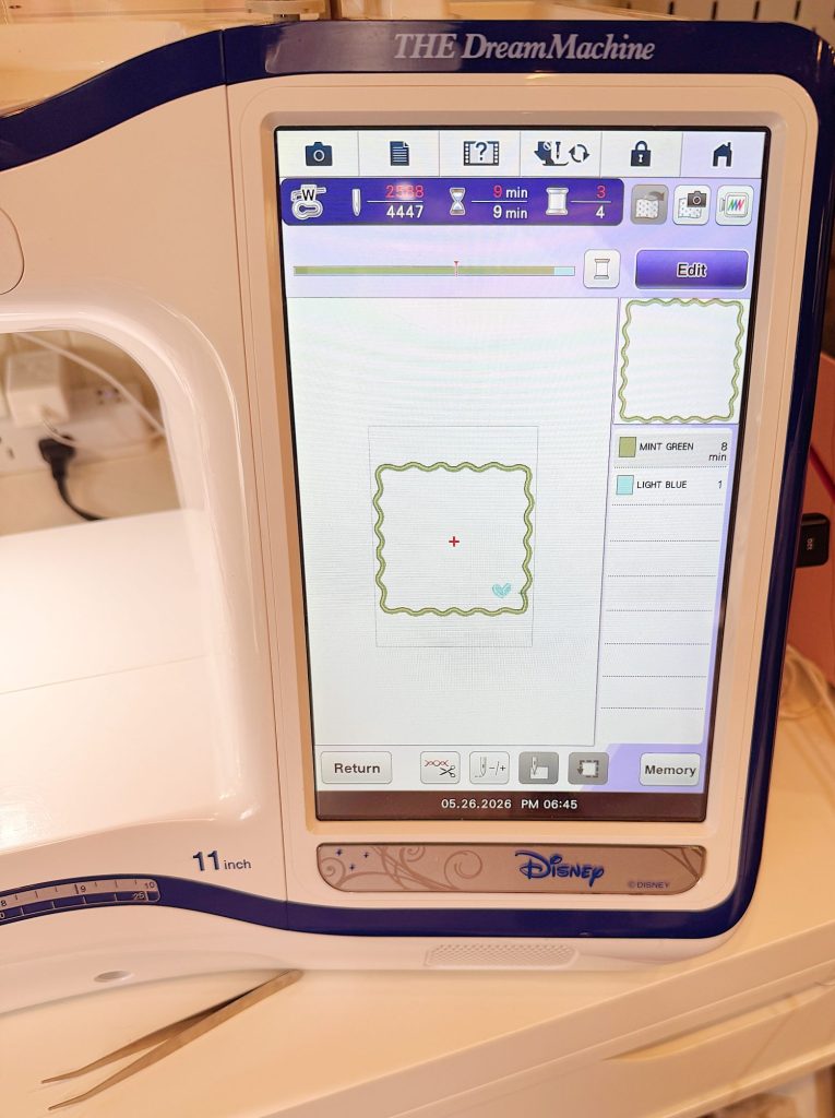 Close-up of a digital embroidery machine screen displaying a scalloped square design. The screen shows stitch settings, design options, and the Disney logo.