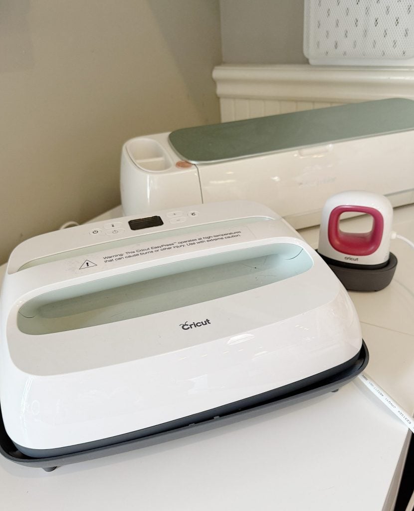 Three Cricut machines are displayed on a white table: a Cricut EasyPress, a Cricut Maker, and a Cricut EasyPress Mini.