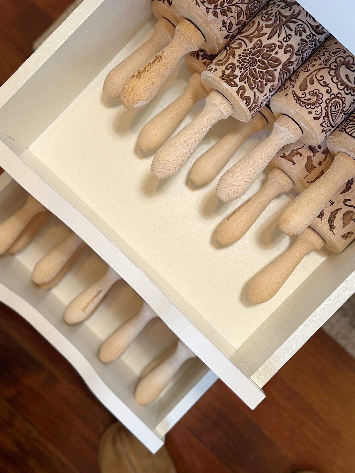 A shelf displaying patterned rolling pins on the top row and plain wooden rolling pins on the bottom row.