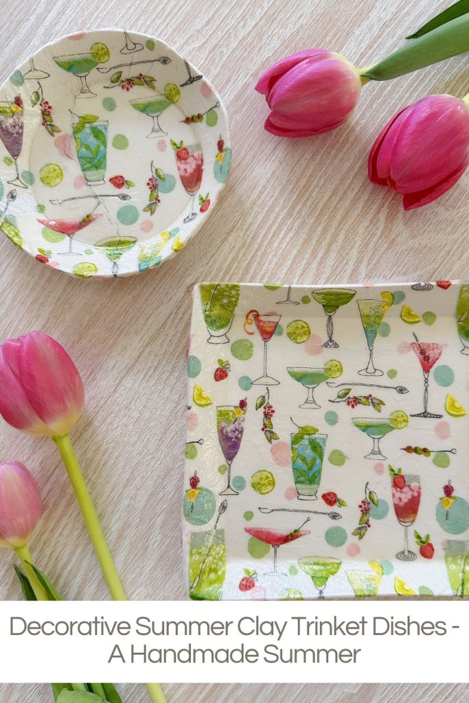Handmade clay trinket dishes with colorful cocktail designs displayed on a wooden surface with three pink tulips.