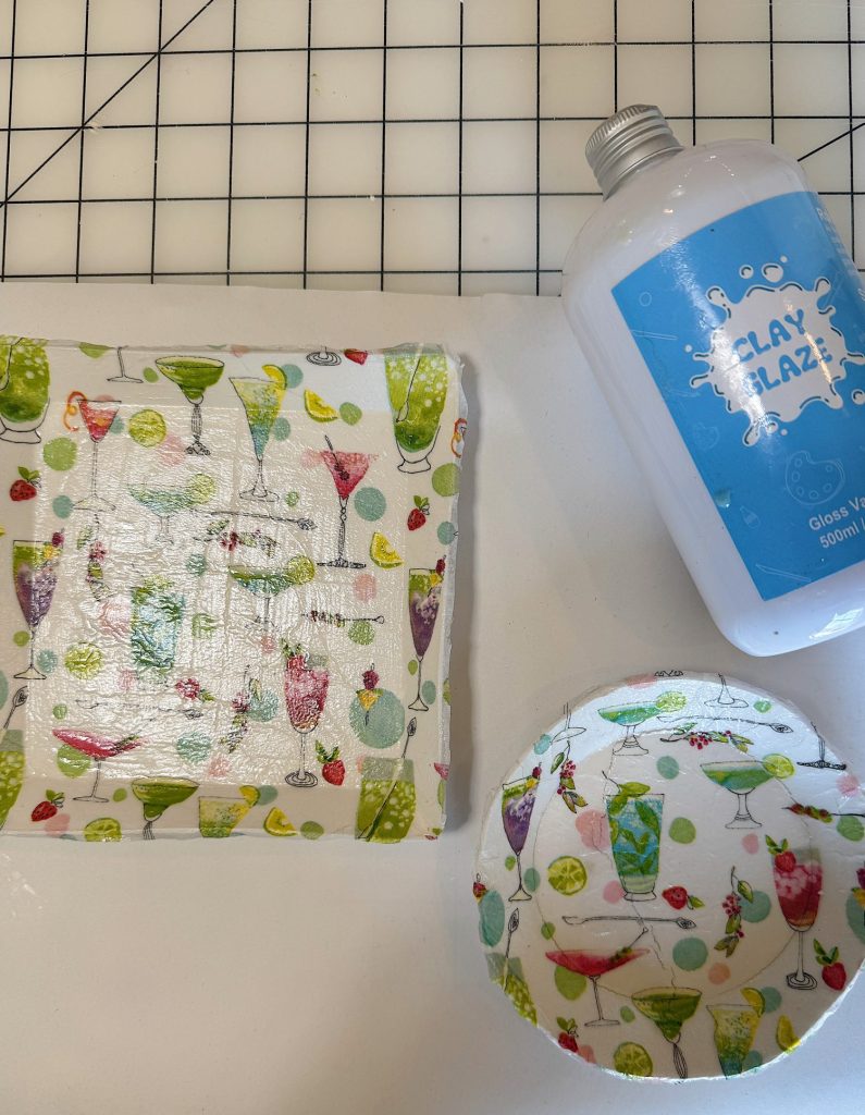 A square and a round dish with a colorful cocktail glass pattern are shown next to a bottle labeled "Clay Glaze" on a white surface with a grid background.