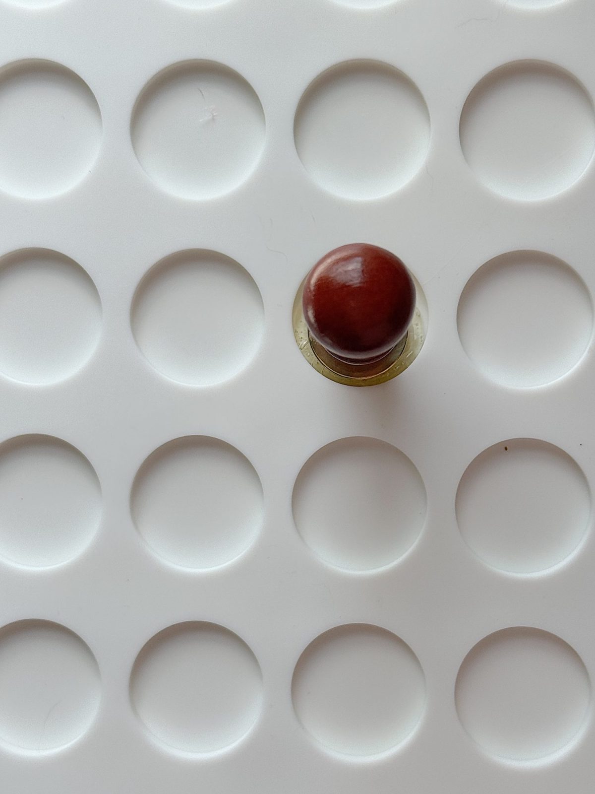 A single brown and brass stamp is placed on a white surface with a grid of circular indentations.