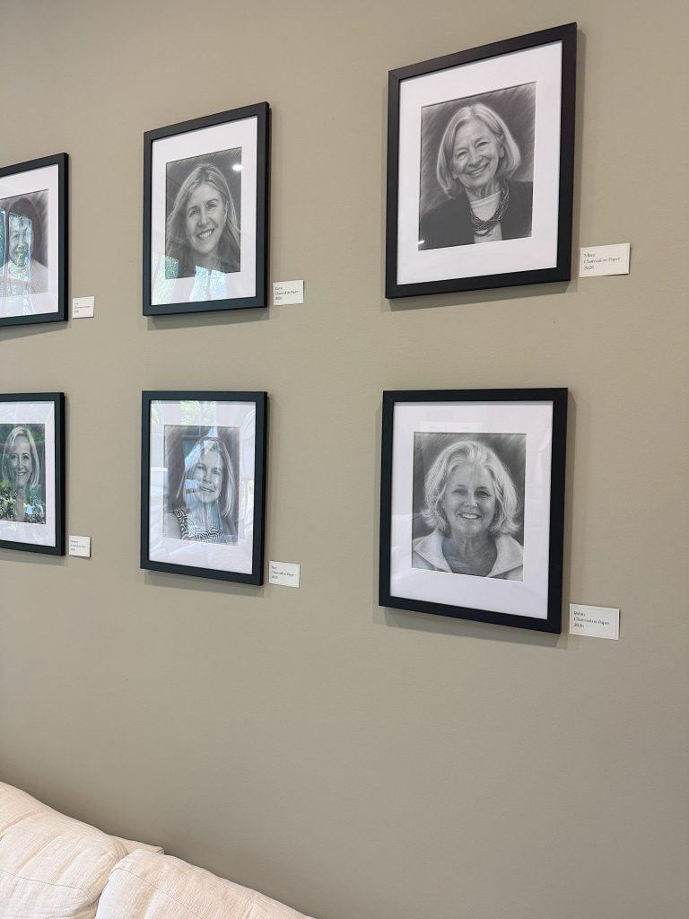 A beige wall displays six framed black-and-white portraits of women, each with a small label beneath, above a light-colored couch.