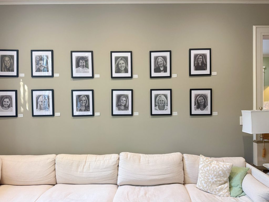 A beige sofa sits against a wall displaying twelve framed black-and-white portraits of women arranged in three rows.