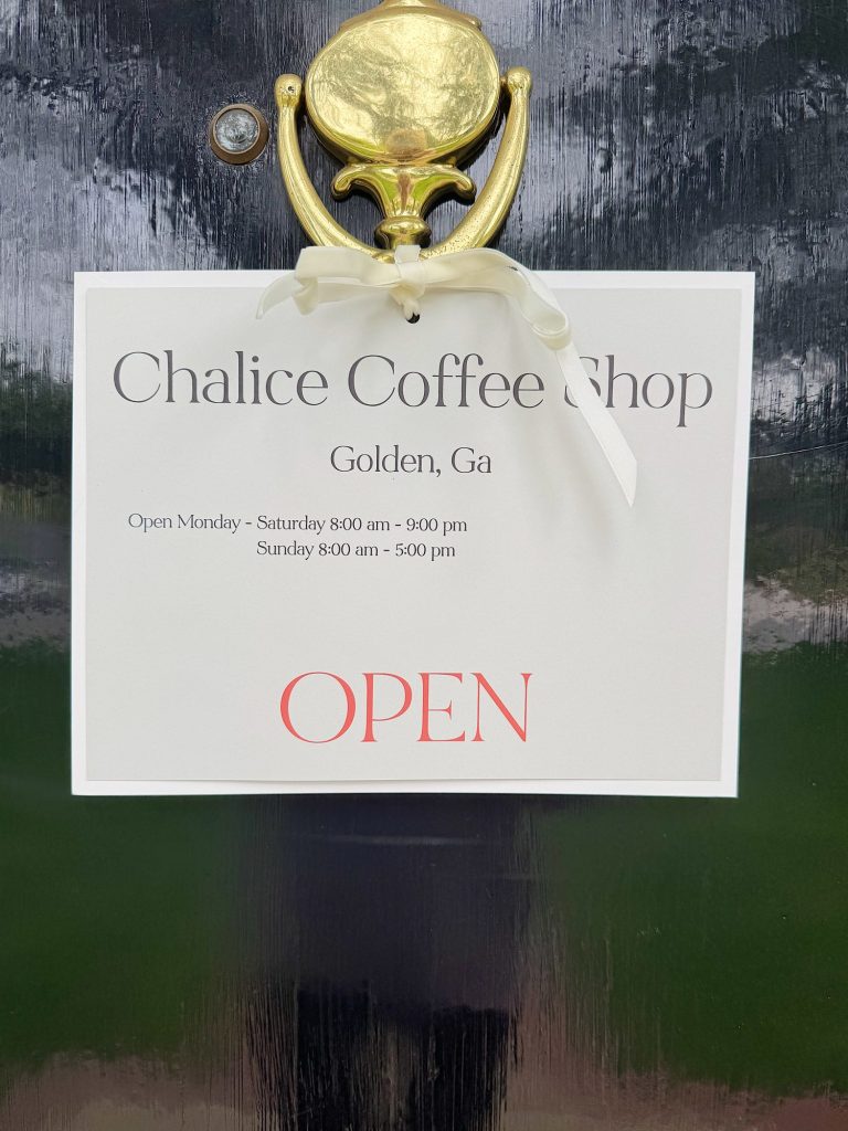 A sign on a door reads "Chalice Coffee Shop, Golden, Ga, Open Monday-Saturday 8 am-5 pm, Sunday 8 am-5 pm" with "OPEN" in large red letters below. A gold door knocker is above the sign.