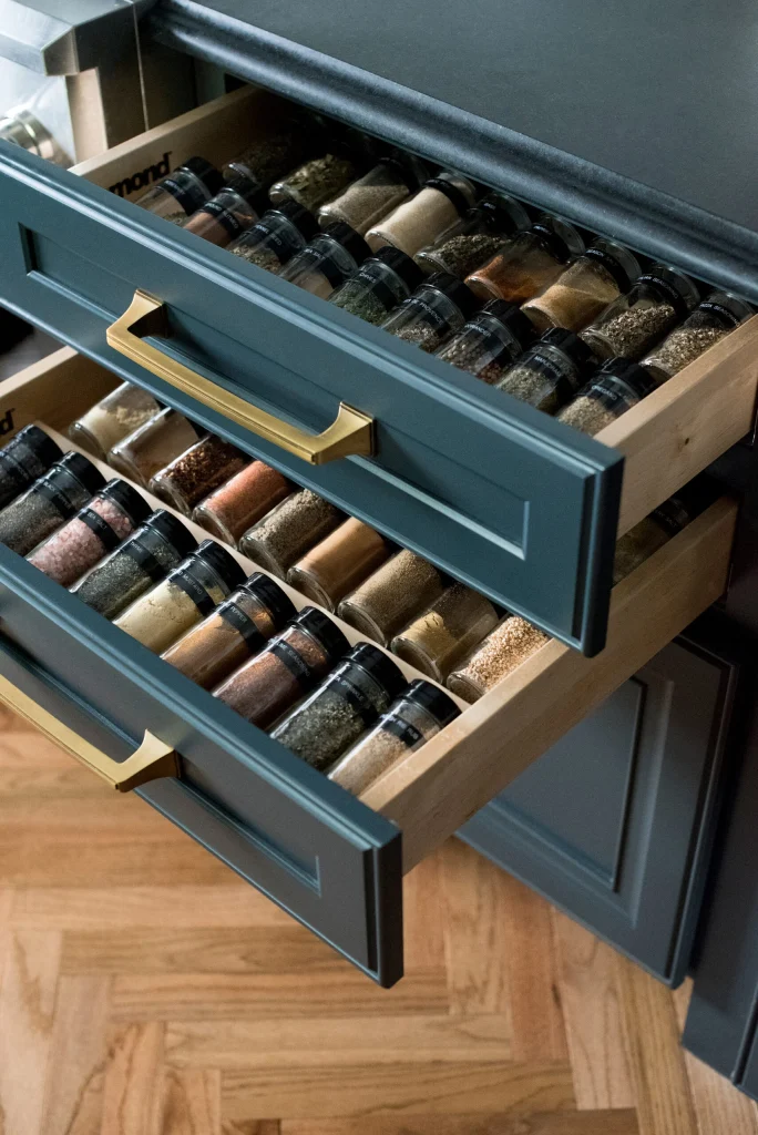 Two kitchen drawers are open, each neatly organized with rows of spice jars arranged by type.