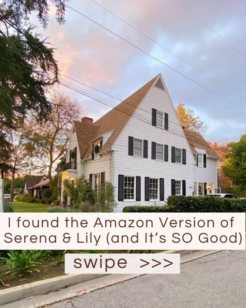 A large white two-story house with dark shutters and steep gabled roof sits on a tree-lined street at sunset; text reads, “I found the Amazon Version of Serena & Lily (and It’s SO Good). Swipe >>>”.