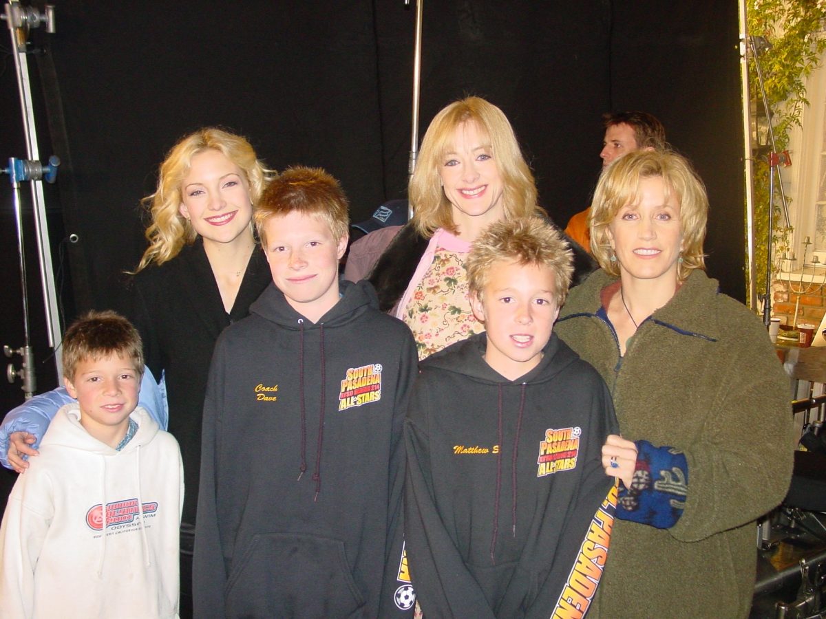 A group of three women and three boys pose for a photo indoors; the boys wear matching hoodies and everyone is smiling.