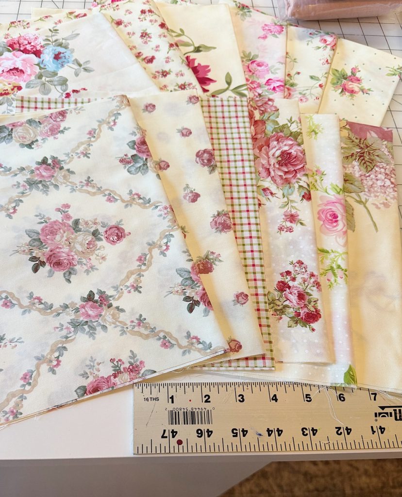 A selection of floral and patterned fabric squares is arranged on a table next to a ruler showing inches.