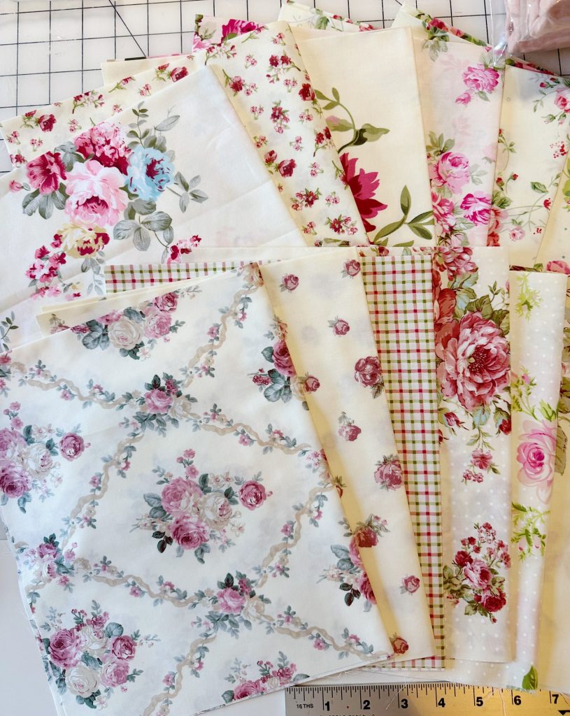 A selection of floral and patterned fabric swatches in pastel colors, arranged overlapping on a table with a ruler visible at the bottom.