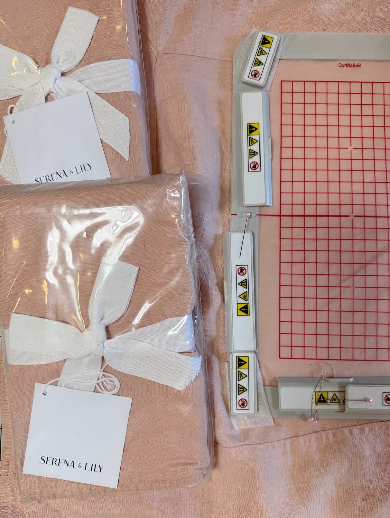 Two packaged pink Serena & Lily cloths with white ribbons are next to a rectangular plastic cutting mat with a red grid and multiple caution stickers.