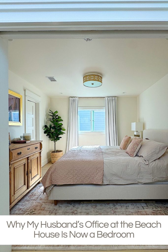 A bright bedroom with a large bed, light bedding, a wooden dresser, a potted plant, and a window with white curtains.
