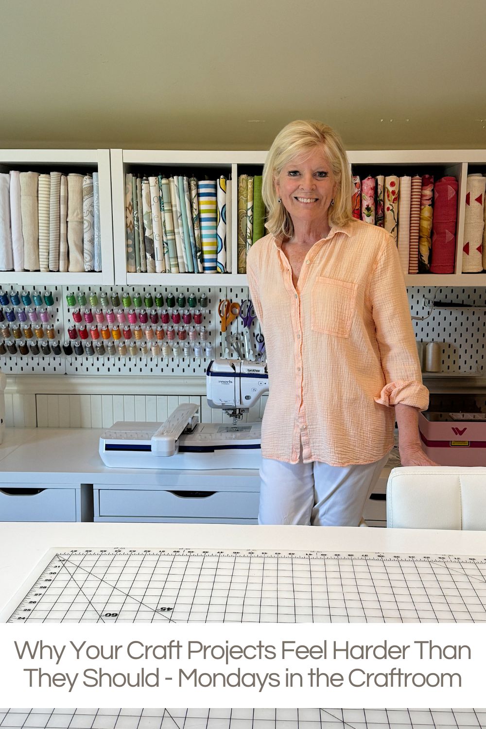A woman stands in a well-organized craft room with shelves of fabric, thread spools, a sewing machine, and a cutting mat.
