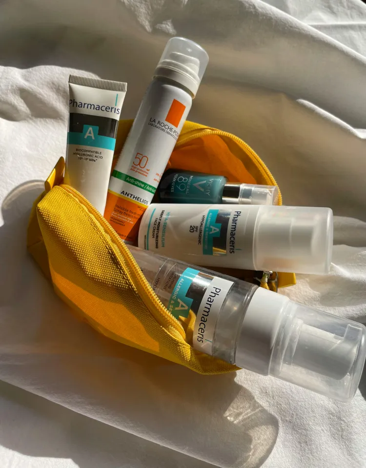 A yellow zippered pouch containing various skincare products, including Pharmaceris and La Roche-Posay bottles and tubes, displayed on a white fabric background.