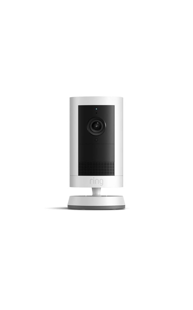 A white Ring indoor security camera is shown centered on a plain white background. The camera features a black lens area and sits on a round base.
