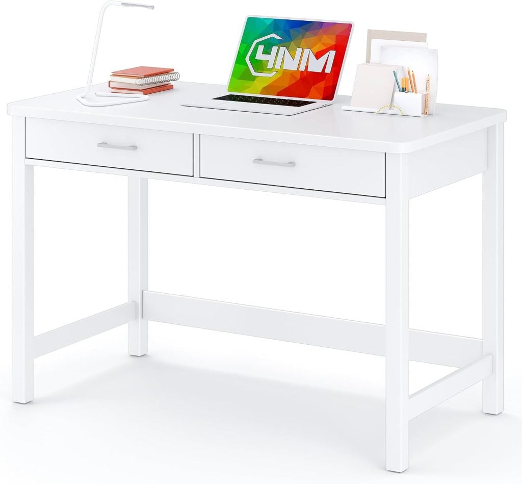 A white desk with two drawers holds a laptop, desk lamp, books, paper tray, and cup with pencils and pens.