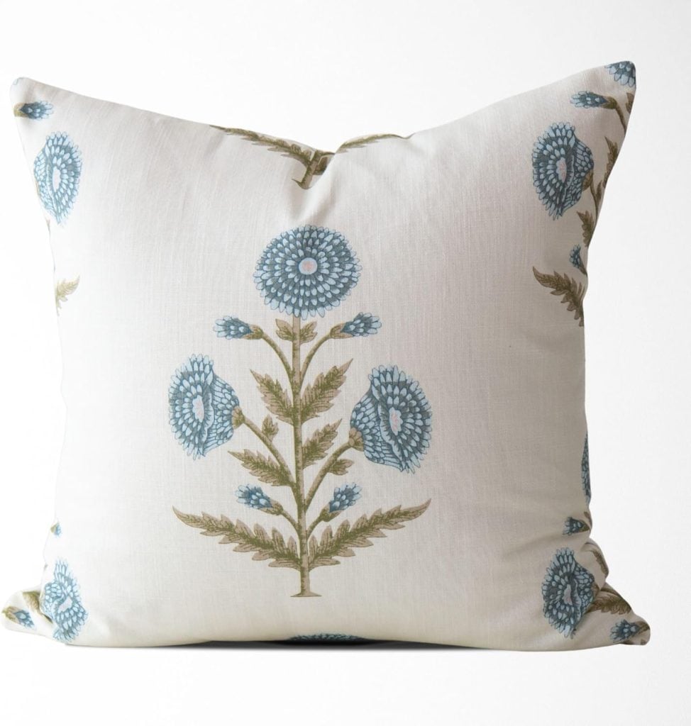 Square decorative pillow with a white background, featuring a symmetrical pattern of blue and green floral designs.