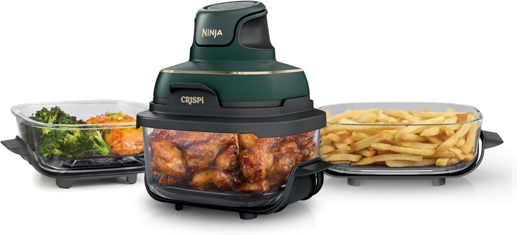 A Ninja air fryer with cooked chicken wings inside, flanked by two glass trays containing broccoli with salmon and French fries.