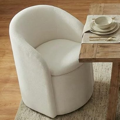 A wooden dining table set for four with beige plates and glasses, surrounded by four white upholstered chairs on a light rug in a softly lit dining room, showcasing the elegant touch of interior designers.