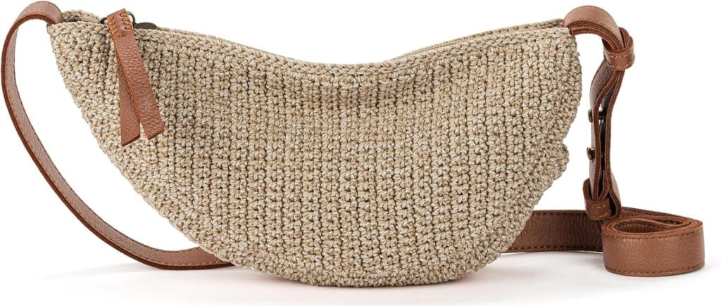 A woven straw half-moon crossbody bag with a brown leather strap and zipper pull, displayed on a white background.