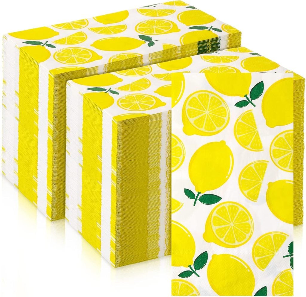 Stacks of paper napkins with a lemon and lemon slice pattern in bright yellow and green on a white background, perfect for pairing with cheerful polymer clay charms at your next summer gathering.