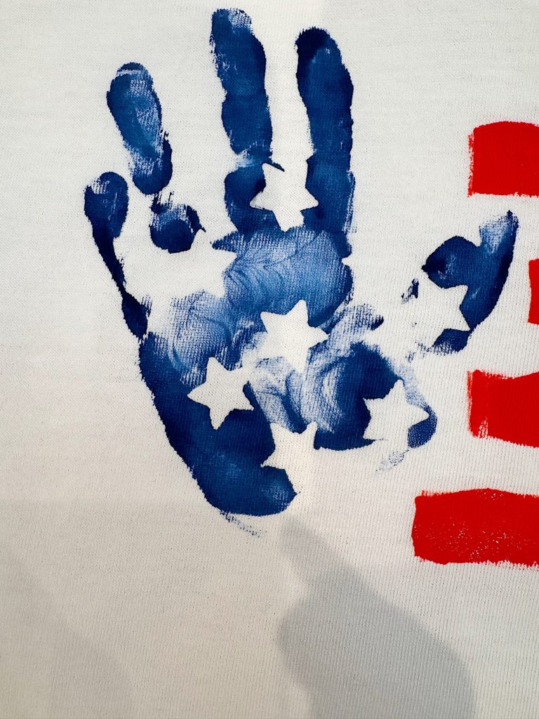 A blue handprint with white stars is next to red stripes, resembling elements of the American flag, on a white background.