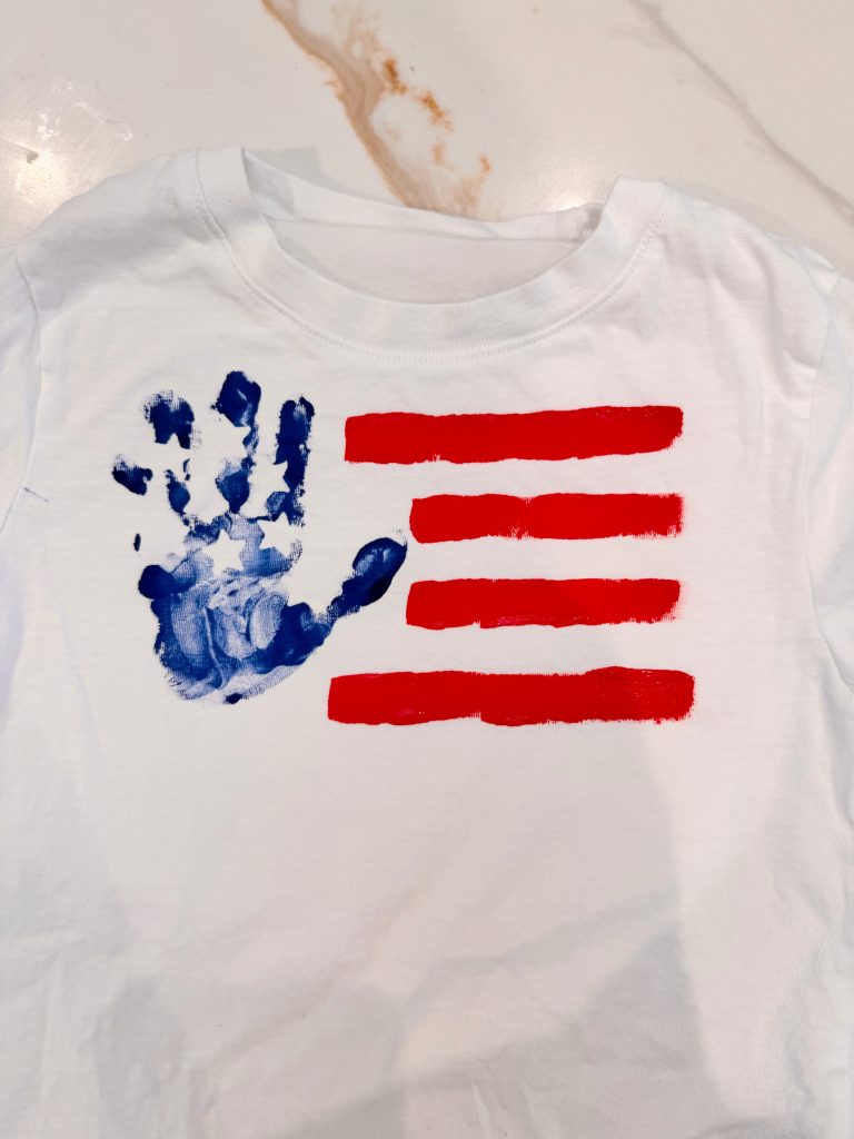 A white shirt with a blue handprint and four horizontal red stripes, arranged to resemble the American flag.