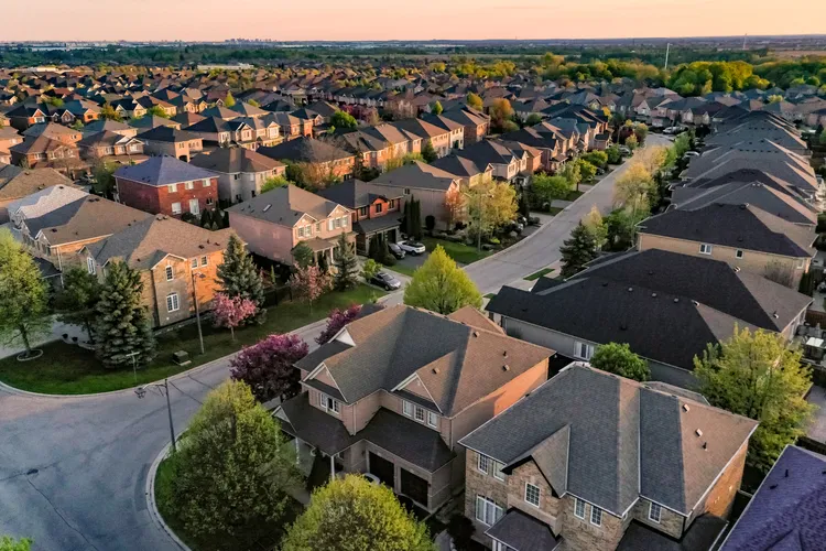 Aerial view of a suburban neighborhood with rows of houses, tree-lined streets, and greenery during sunset.