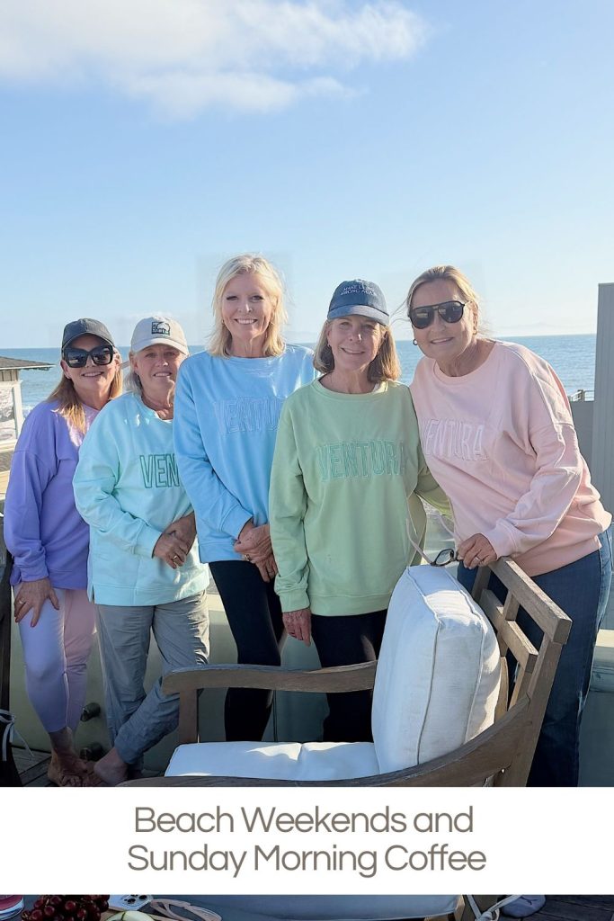 Five women wearing pastel sweatshirts and hats stand together on a deck by the ocean, smiling at the camera. Text below reads, "Beach Weekends and Sunday Morning Coffee.