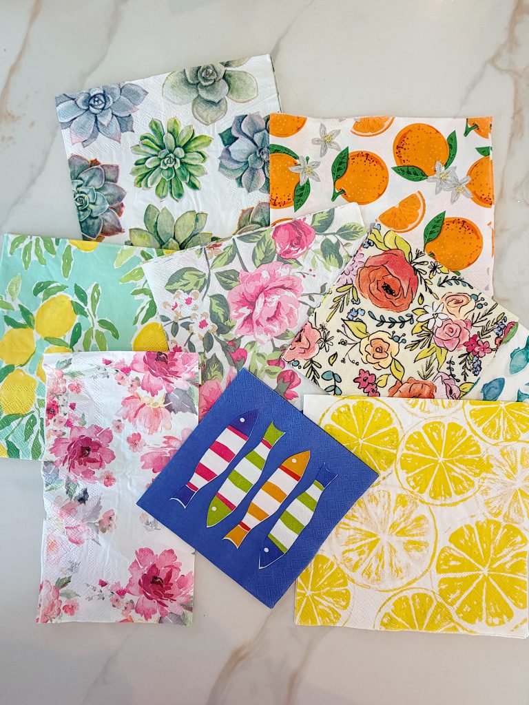 An assortment of decorative paper napkins with various floral, fruit, and fish patterns arranged on a marble surface.