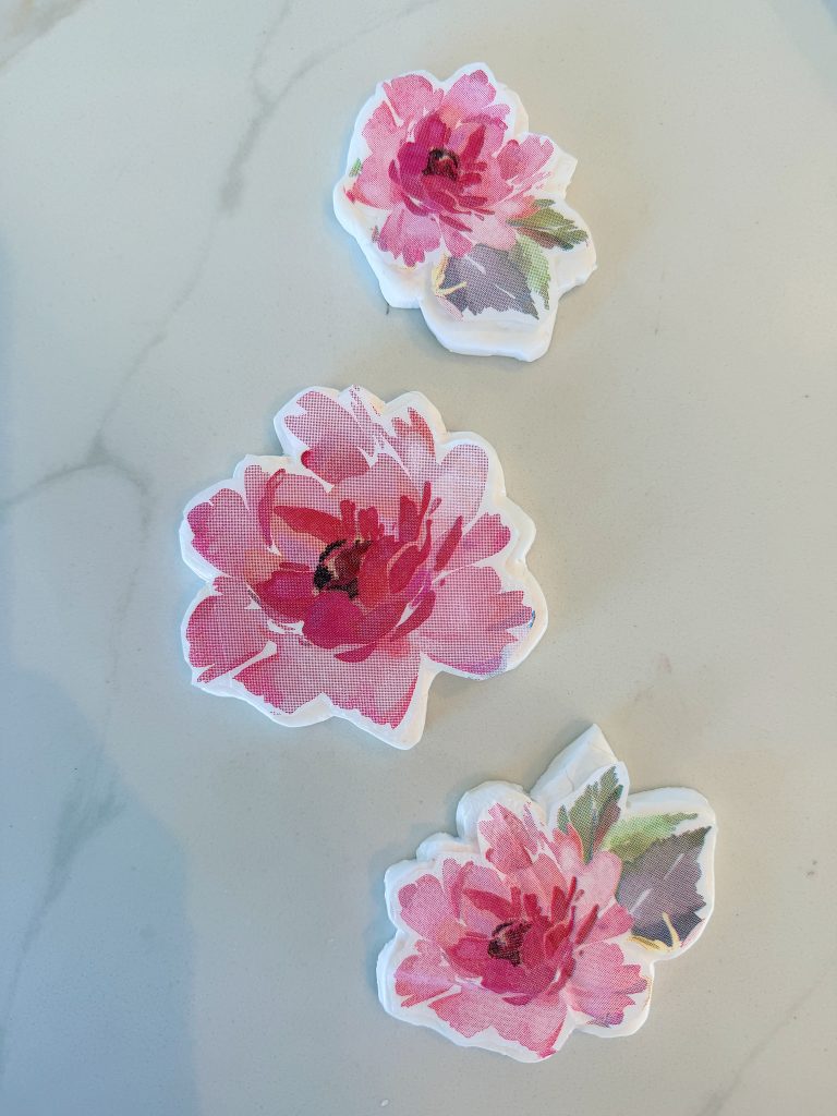 Three decorative stickers featuring pink flowers with green and gray leaves are arranged on a light, marble-patterned surface.