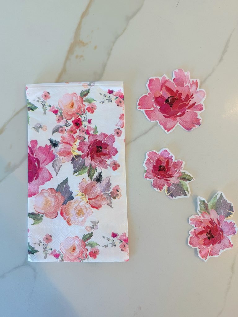 A floral-patterned napkin and three matching floral cutouts are arranged on a light marble surface.