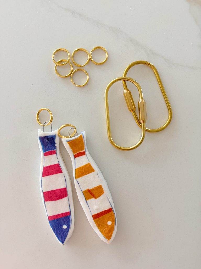 Two key rings, six small gold rings, and two fish-shaped charms with colorful stripes are arranged on a white surface.