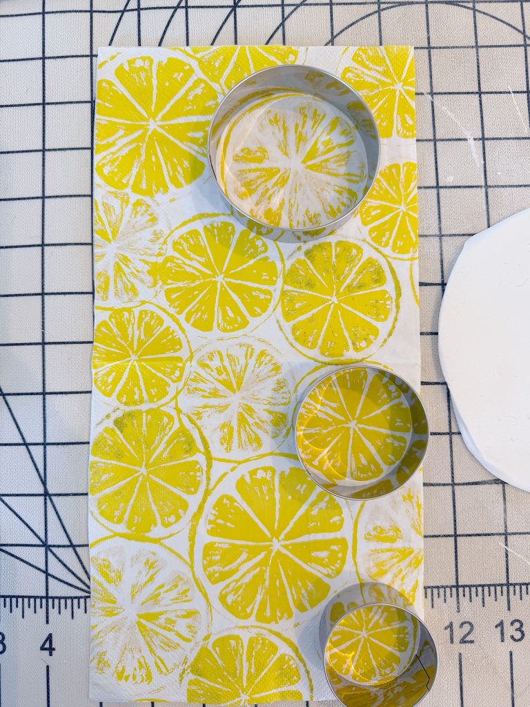 Three metal cookie cutters rest on a napkin with a yellow lemon slice pattern, on top of a grid-patterned cutting mat with visible measurement markings.