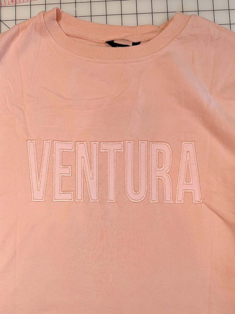 A light pink sweatshirt with the word "VENTURA" embroidered in large, capital letters across the chest.