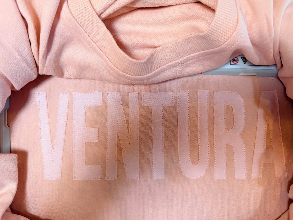 A light pink sweatshirt with the word "VENTURA" printed in large, bold, white letters on the front.