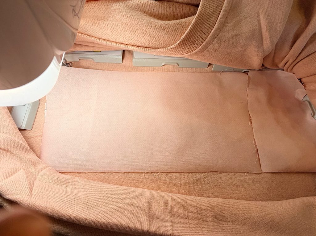 A pink fabric is hooped and placed in an embroidery machine, ready for stitching, with stabilizer visible underneath.