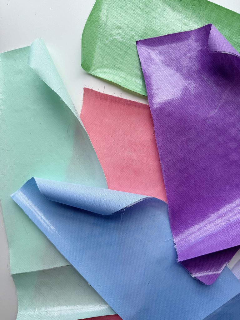 Several pieces of fabric in pastel colors—light blue, pink, green, and purple—are layered and overlapping on a white surface.