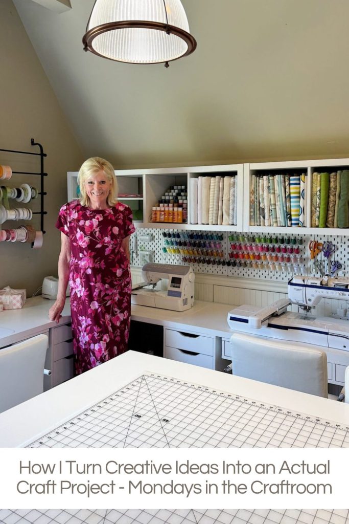 A woman in a floral dress stands in a well-organized craft room with shelves of supplies, a sewing machine, and a large workspace table.