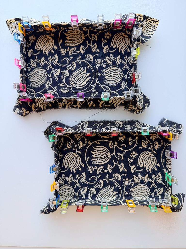 Two dark blue fabric trays with a white floral pattern, edges folded up and secured with colorful sewing clips, are placed on a white surface.