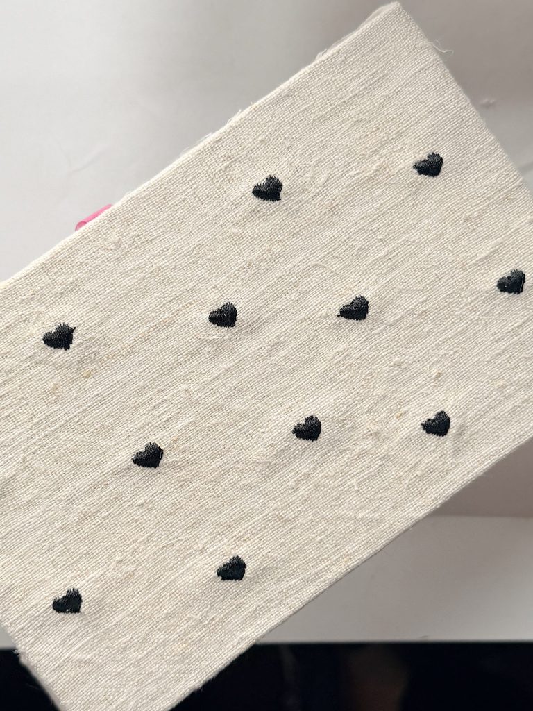 A rectangular piece of off-white textured fabric with a pattern of small black heart shapes arranged in rows.