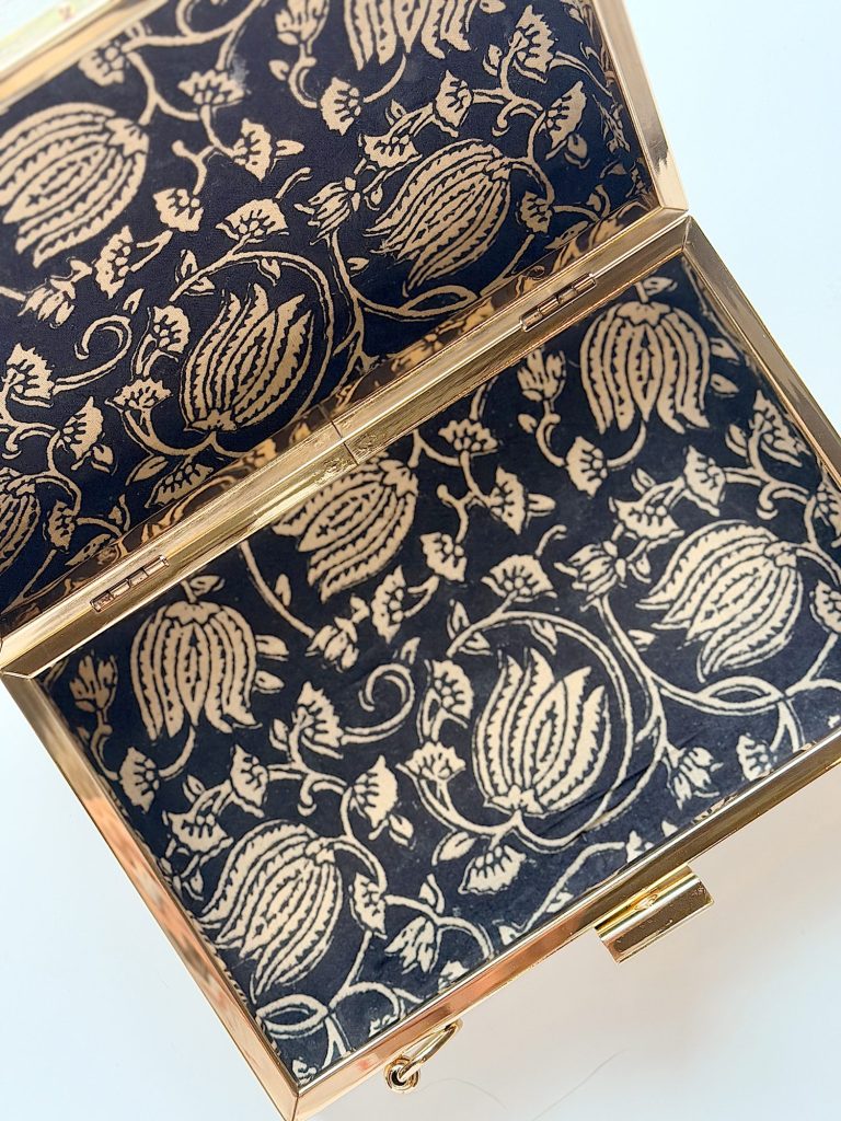 A rectangular box with a gold frame and fabric lining featuring a cream floral pattern on a dark background.