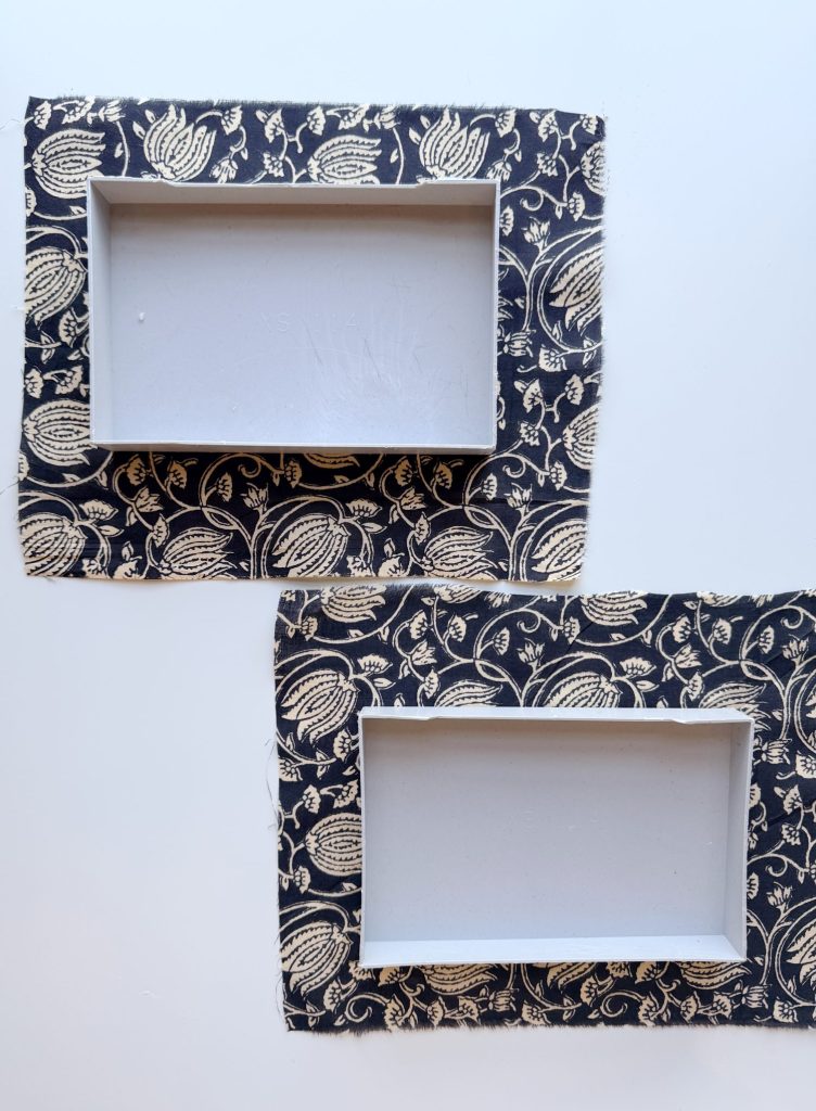 Two rectangular trays with white interiors and black fabric exteriors featuring a beige floral pattern, placed side by side on a white surface.