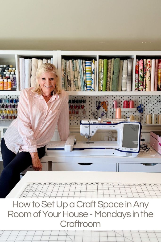 A woman stands next to a sewing machine in a craft room with fabric, thread, and supplies neatly organized on shelves.