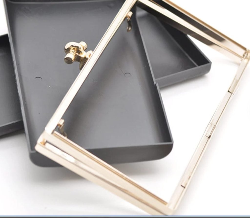 A close-up of a black rectangular case with a detached gold metal frame and clasp placed on top.