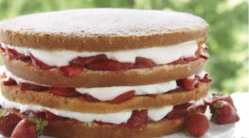 Three-layer sponge cake filled with whipped cream and sliced strawberries, with whole strawberries placed beside the cake.
