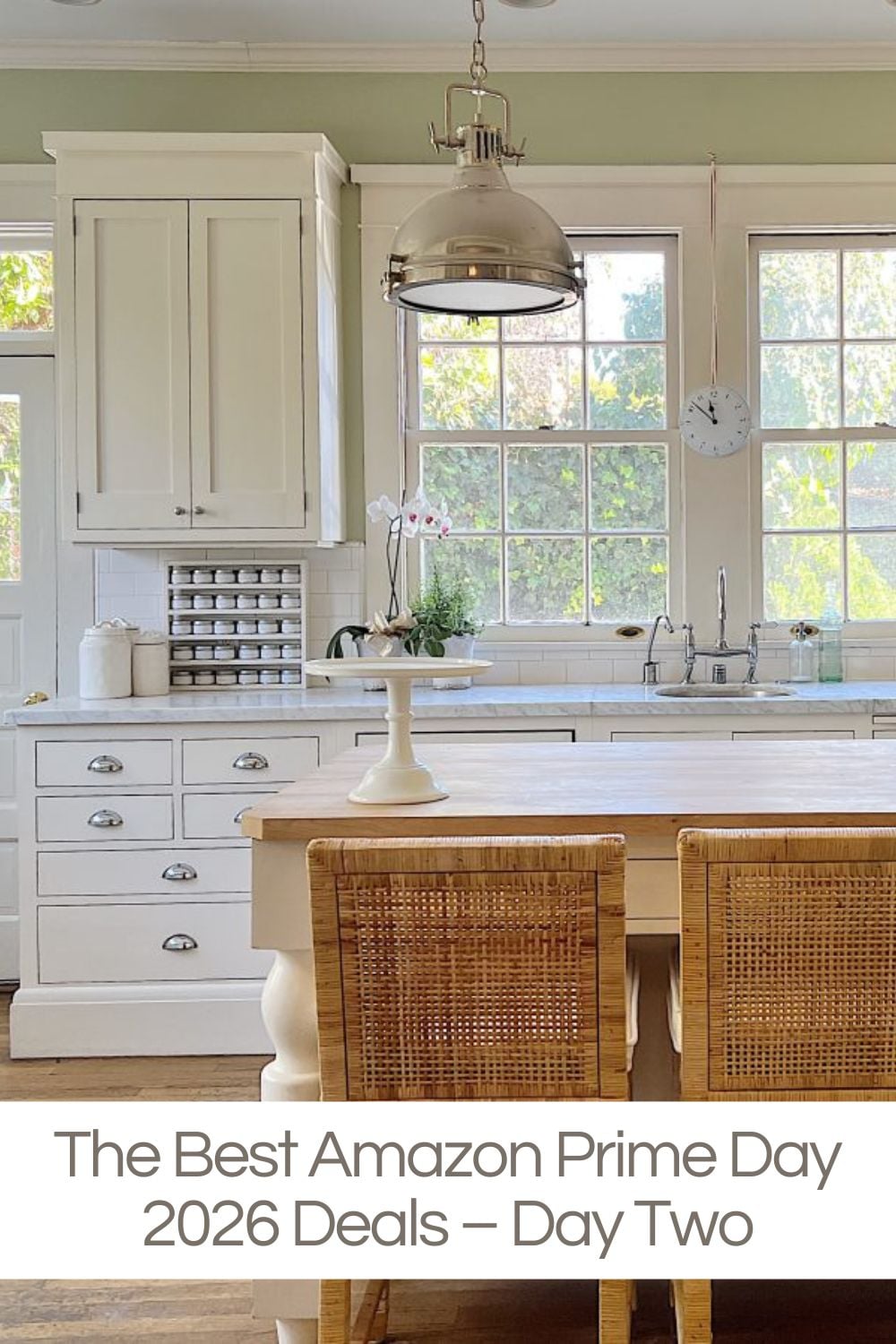 A bright kitchen with white cabinets, a wooden island, two woven chairs, pendant light, and large windows; text overlay reads “The Best Amazon Prime Day 2026 Deals – Day Two.”.