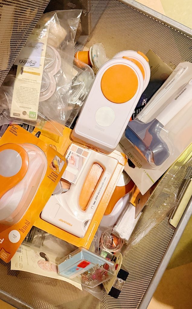 A mesh bin filled with various packaged household gadgets, including orange and white lint removers and other small tools in plastic and cardboard packaging.